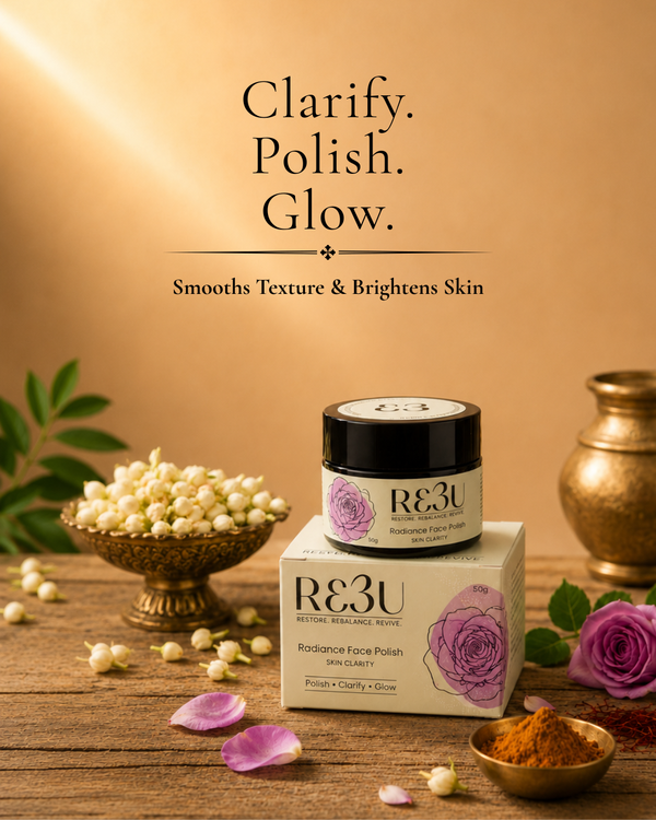 R3U Radiance Face Polish in a black jar with a purple rose illustration, displayed on top of its cream-colored box. The scene is styled with a wooden table, a bowl of jasmine flowers, rose petals, and a brass pot against a warm beige background with the text 'Clarify.